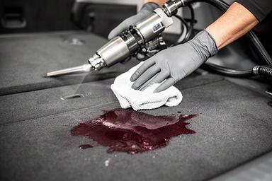 ワインの染みが付いた車の荷室を専用機材で処理するスタッフの手元